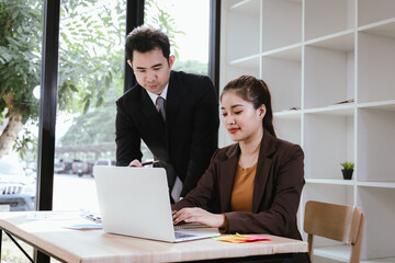 Young Asian man and woman discussing work in office using laptop computer. Businessman and businesswoman.