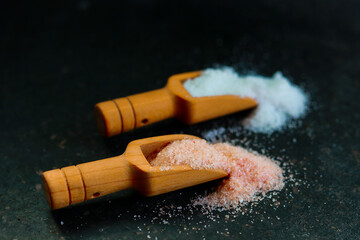 Pink salt and sea salt in wooden scoop on black background, selective focus,