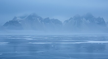 A frozen landscape with an icy lake in the foreground and mist-covered mountains in the background, creating a serene and mysterious atmosphere.