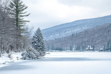 Obraz premium Frozen lake surrounded by snow-covered trees and mountains during winter