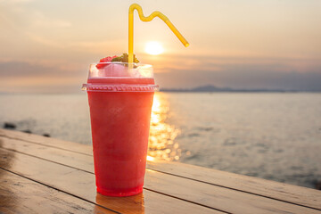 Watermelon smoothie on a wooden table with a beautiful sunset sea backdrop