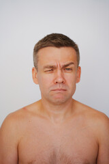 Obraz premium Portrait of a grimacing middle-aged man with a naked torso on a white background. photo posing. men's physical and mental health 