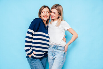 Two young beautiful smiling brunette hipster female in trendy summer clothes. Lovely women posing on blue background in studio. Positive models having fun. Cheerful and happy. isolated