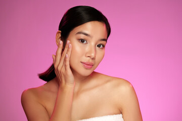 Woman applying skincare product with a soft expression under pink light