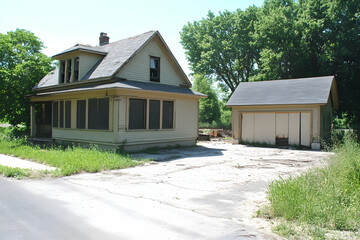 Derelict house and detached garage needing renovation, overgrown yard.  Ideal for real estate, renovation, or abandoned property themes.