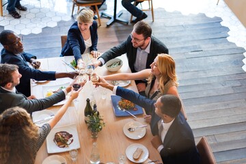 Group of diverse people enjoying meal together, toasting with wine glasses around a dining table,...