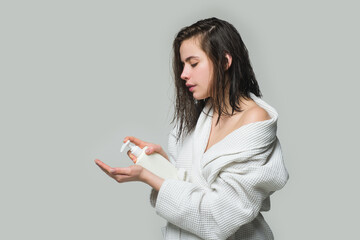 Fototapeta premium Girl with beautiful straight hair is trying new shampoo. Woman holding a bottle shampoo on studio background. Young woman with shiny hair holding bottle with shampoo.