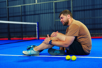 Man sits on blue tennis court holding ankle after injury during match
