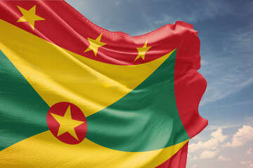 Waving flag of Grenada in blue sky. Grenada flag on pole for Independence Day. The symbol of the state on wavy fabric.