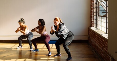 Three women exercising indoors, performing squats. Diverse group in activewear, focusing on...