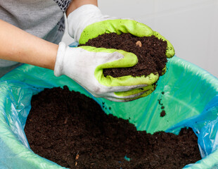 A person wearing a green glove is holding a bag of dirt