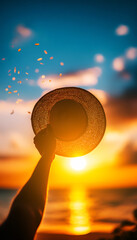 Hand holding hat against vibrant sunset sky with colorful clouds and ocean in background, capturing a summer vibe.