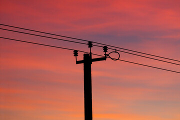 A power line pole is silhouetted against a beautiful sunset