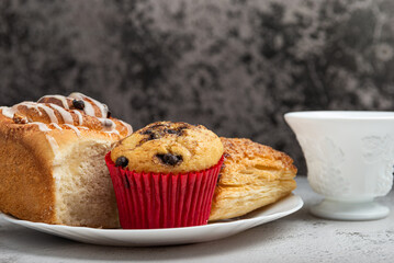 Close-up of a white plate with different freshly baked desserts, cinnamon roll, cupcake, and a sweet pastry.