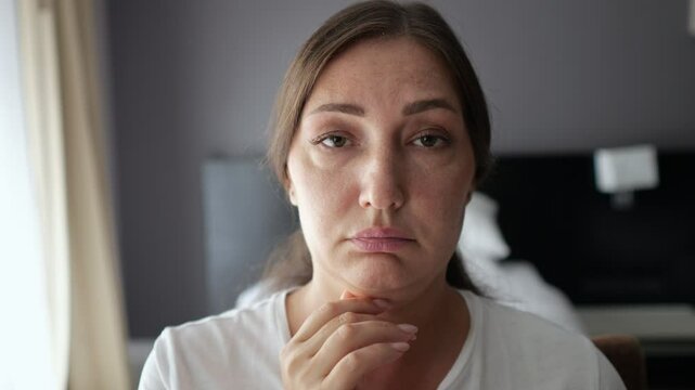 Woman examines neck sagging skin looking closely in mirror