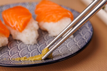 Hand dipping salmon onigiri into soy sauce with chopsticks on a gray table with a brown mat and...