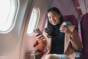 Successful businesswoman counting money and using smartphone while traveling on airplane, enjoying...