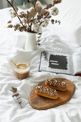 Eclairs, coffee, open book, dried flowers. Breakfast in bed