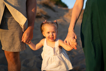Little toddler girl at beach holding parents hands
