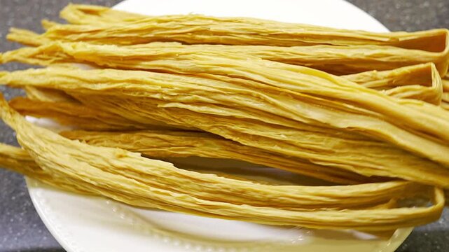 The dried semi-finished soy asparagus on a white plate. Fuzhu. soy milk foam formed during the boiling process of soybeans. rotation