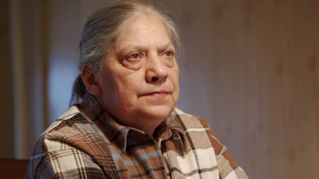 elderly woman, with a hint of mischief in her eyes, warmly engages in a conversation with someone off-camera. Her facial expression conveys a sense of joy and a possible sharing of cherished memories