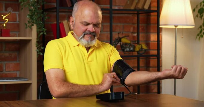 Indian senior man checks blood pressure at home with a digital monitor, sees normal reading, and smiles while holding a pill bottle for routine health care