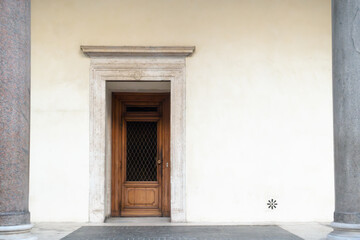 Old wooden door on an white plaster wall of medieval stone building between two gray columns 