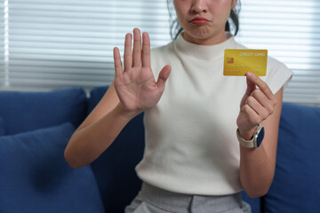 Young woman showing stop gesture with hand while holding credit card, expressing refusal of excessive spending and financial problems concept