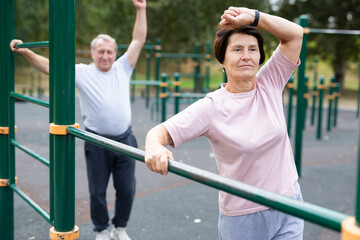 Obraz premium Healthy lifestyle in retirement - an elderly woman does a workout on the sports ground in park.