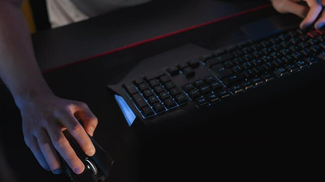 Gamer plays video game at computer club, fingers click on buttons of gaming mouse, keyboard with RGB lighting. Professional E-sport tournament, Cyber team. Real-time strategy shooter. Modern equipment