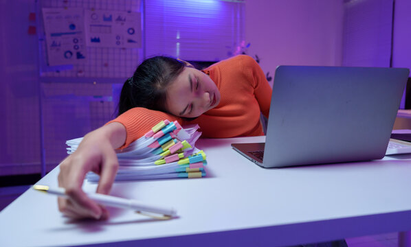 Overworked individual asleep at a desk, surrounded by a laptop and stacks of documents, highlighting workplace fatigue and burnout in a modern office environment - Powered by Adobe
