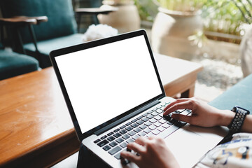 A person typing on a laptop with a blank screen in a cozy seating area featuring wooden tables and...