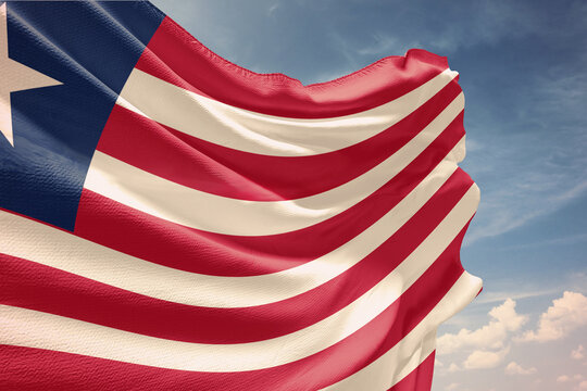 Waving flag of Liberia in blue sky. Liberia flag on pole for Independence Day. The symbol of the state on wavy fabric.