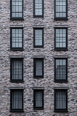 Fototapeta premium Urban brick building with large black-framed windows showcasing modern architecture in a dense city environment during a cloudy day