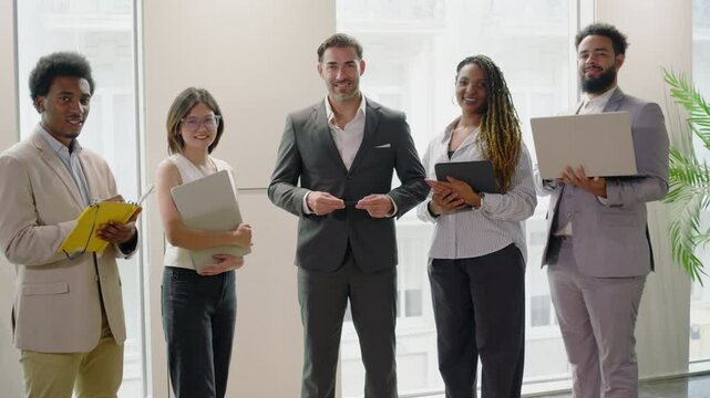 Diverse group of highly skilled professionals stands in a row in modern office. Multiethnic professional employees executives group posing together for corporate portrait, leadership. Slow motion