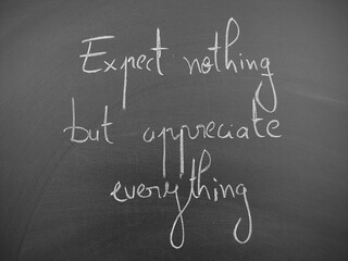 Obraz premium Expect nothing but appreciate everything motivational quote written on a black chalkboard background
