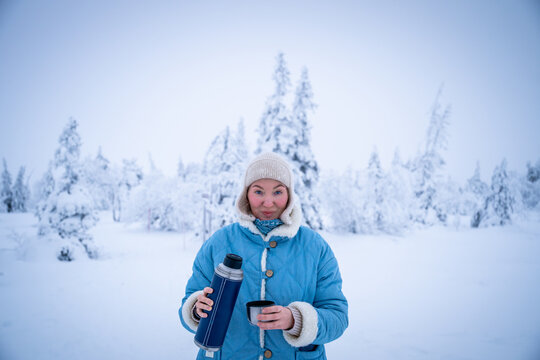 Woman pouring a hot drink from a thermos into a cup in winter forest