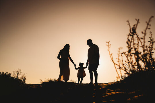 Silhouette family beach pregnant mom dad little girl holding hands