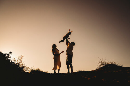 Silhouette family beach pregnant mom dad throwing girl air