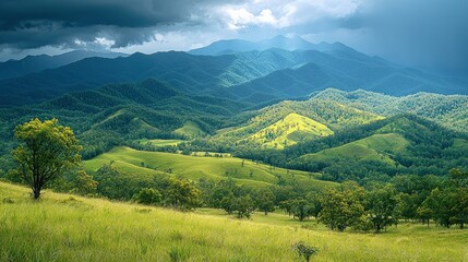 Obraz premium Scenic view of rolling green hills and distant mountains under dramatic sky.