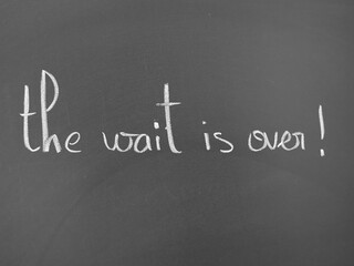Fototapeta premium The wait is over written in white chalk on a dark background
