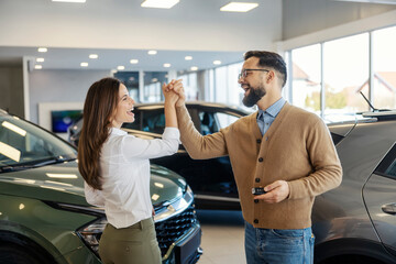Naklejka premium Happy buyer couple giving high five for car purchase at car showroom.