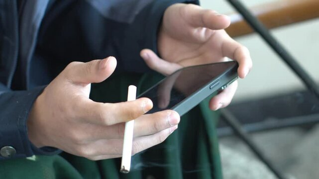 Close up of hand holding cigarette and smartphone