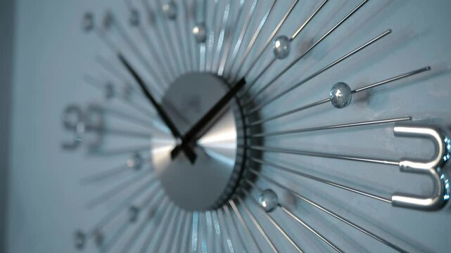 On the white wall there is a modern beautiful stylish chrome mechanical clock with hands, always showing the exact time. Closeup. Shot in motion