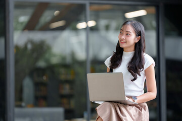 Confident young woman in a casual setting using a laptop. She is focused and engaged, representing modern technology and remote work in a bright, outdoor environment