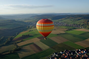 Obraz premium A colorful hot air balloon drifting over a countryside valley filled with patchwork fields