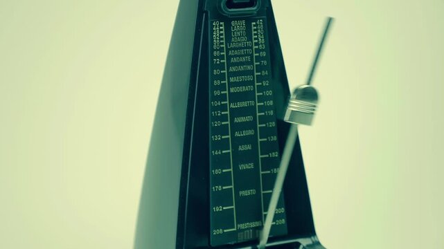 New, modern, shiny, black metronome, with a swinging pendulum, accurately beats in time, helping the musician not to lose the rhythm, on a light background. Closeup. Macro. Shot in motion