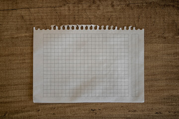 Ripped white graph paper on wooden background. Torn paper background with copy space.