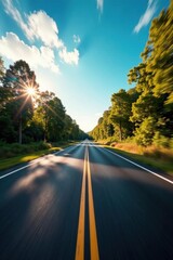 Fototapeta premium A Sunlit Asphalt Road Through a Lush Green Canopy of Trees on a Bright Summer Day