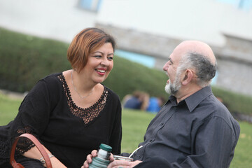  portrait of happy mature couple on the bench in the park talking  and drinking mate